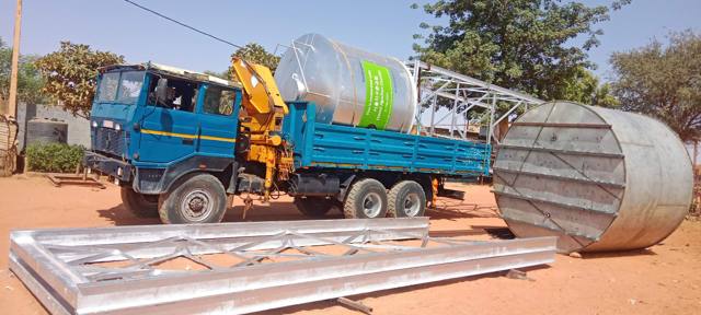 Camion-grue transportant un réservoir inox, avec des éléments de tour au sol